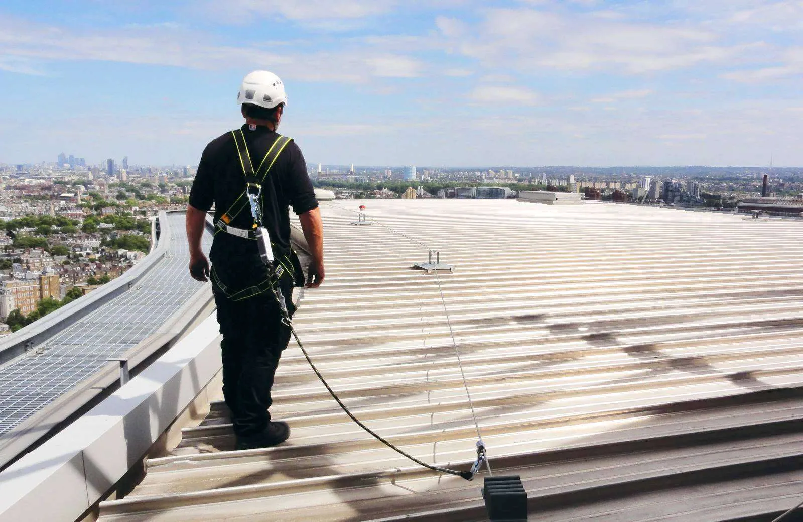 Worker on top of a metal roof, connected to a horizontal lifeline system for aviation fall protection and safe elevated access.